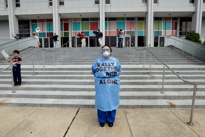 A counter-protester stands on the sidewalk as people with ReopenNC gather in Raleigh, N.C., to press Gov. Roy Cooper to allow businesses to reopen during the COVID-19 outbreak Tuesday, April 21, 2020. (AP Photo/Gerry Broome)
