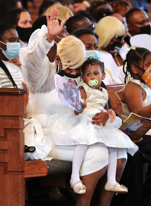 Tomika Miller, the wife of Rayshard Brooks, raises her hand while holding their 2-year-old daughter Memory during a prayer at his funeral in Ebenezer Baptist Church.
